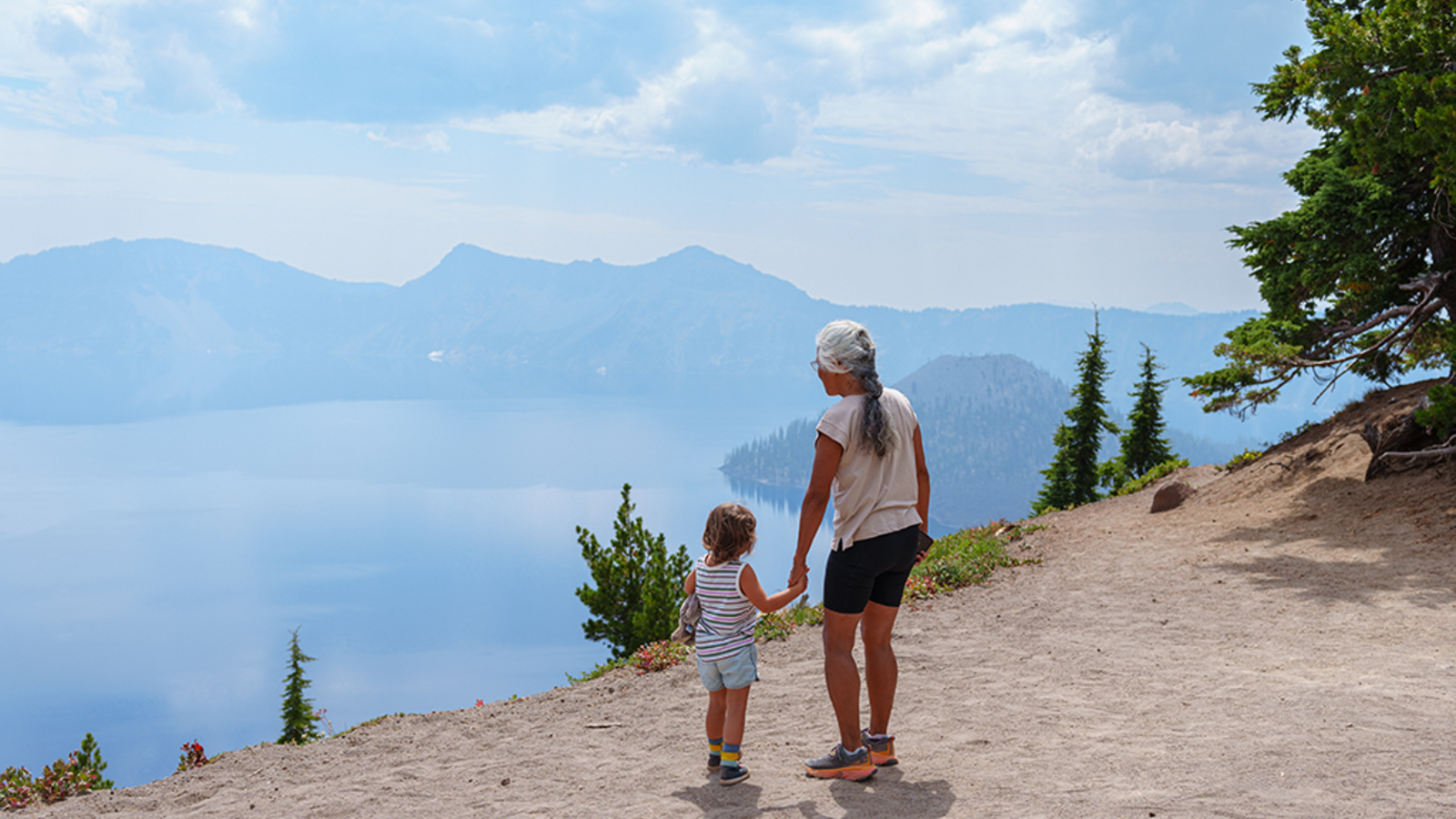 <p>Grandmother and young granddaughter look out to Crater Lake while hiking. Proposed budget cuts of over $1 billion threaten to close approximately 350 national park sites, severely impacting visitor experiences across the country.</p>